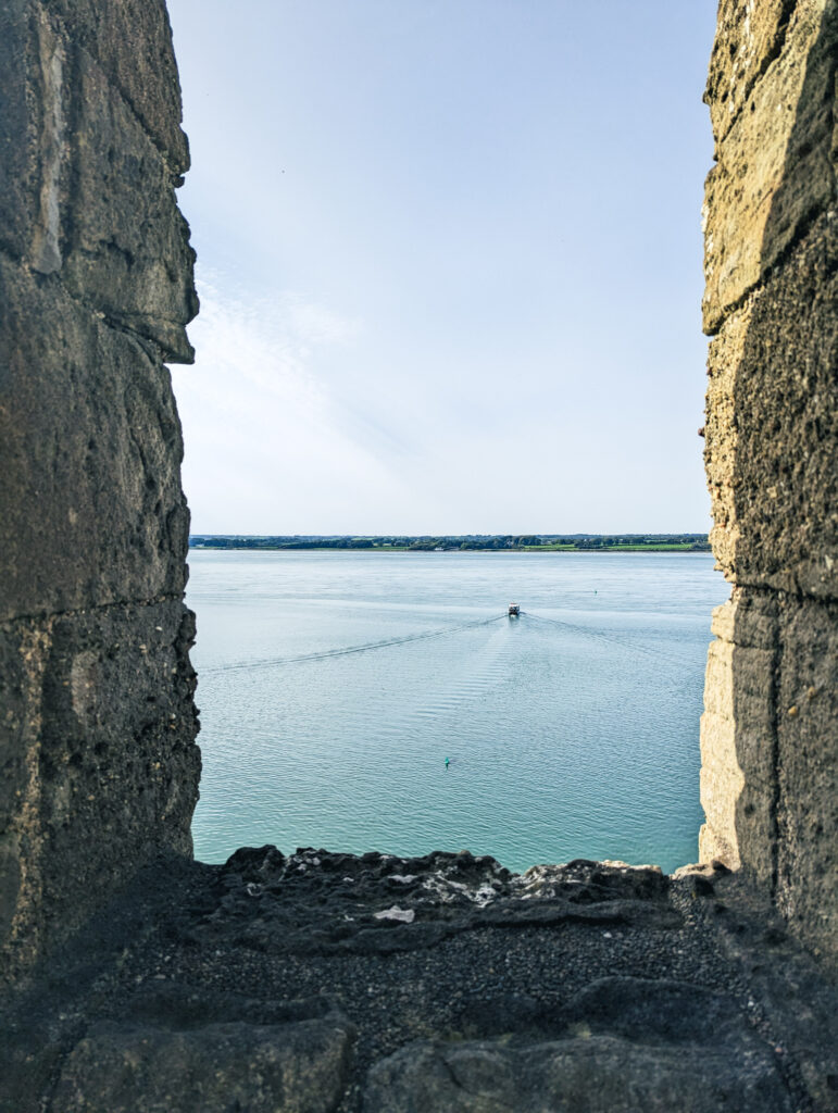 looking out to a boat on the sea from inside Caernarfon Castle